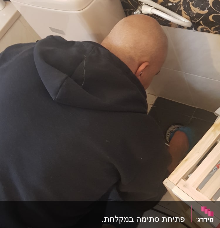 אדם עובד על צנרת ליד אסלה בשירותים